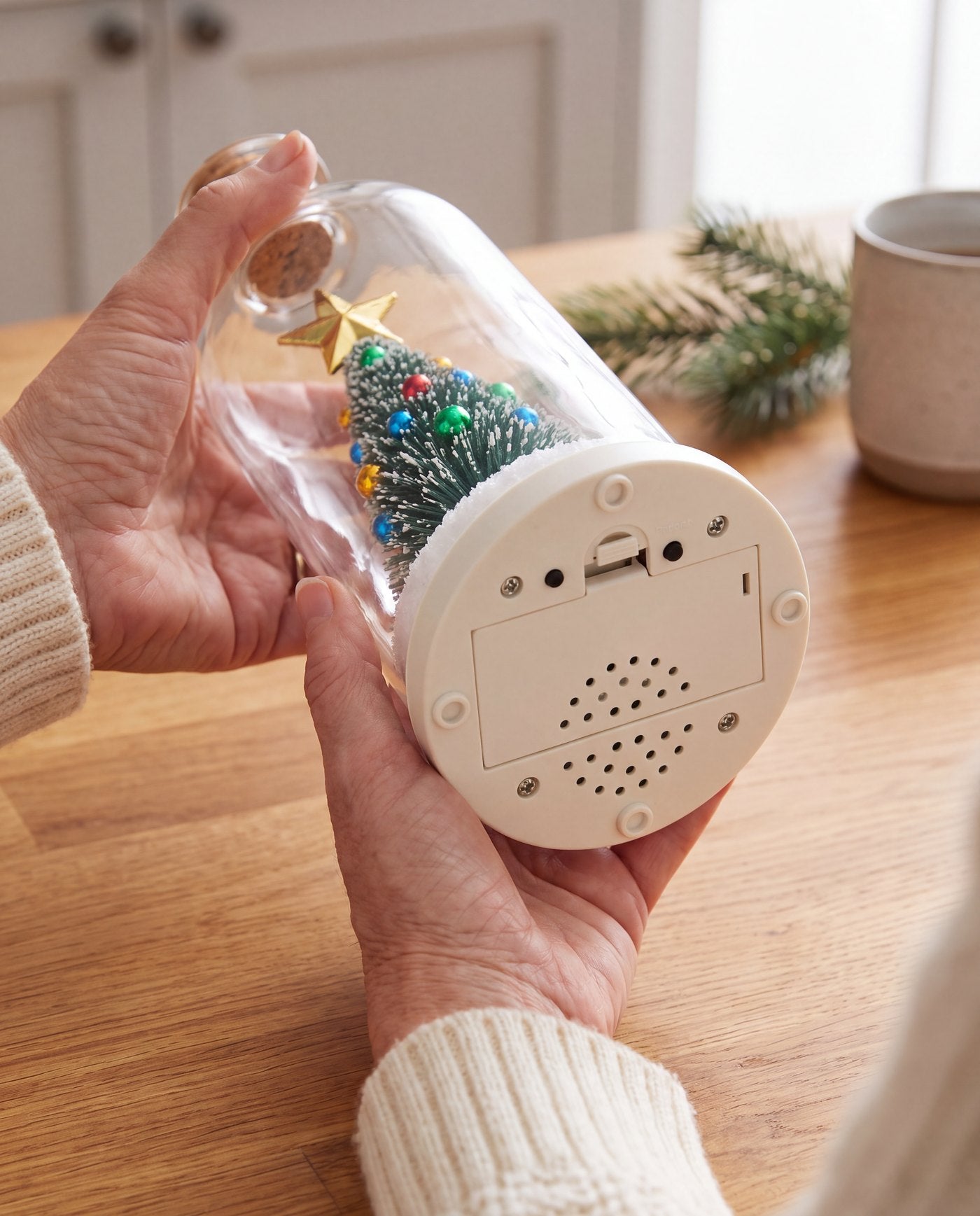 Hands holding the bottle on its side to show the round base: a battery door, two small buttons and a round speaker grille.