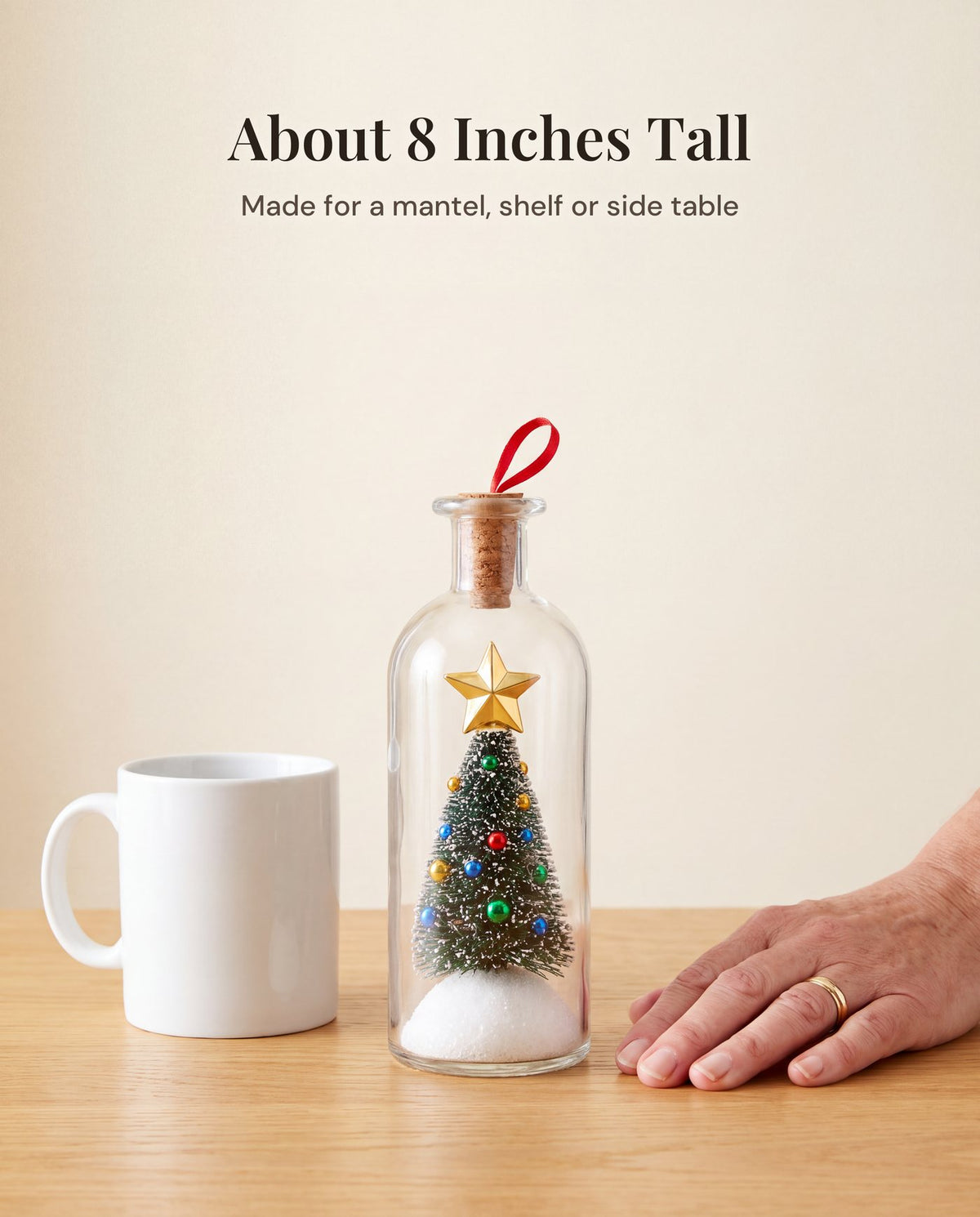 The bottle on a light oak table next to a white mug, about twice the mug's height, with a woman's hand resting beside it.