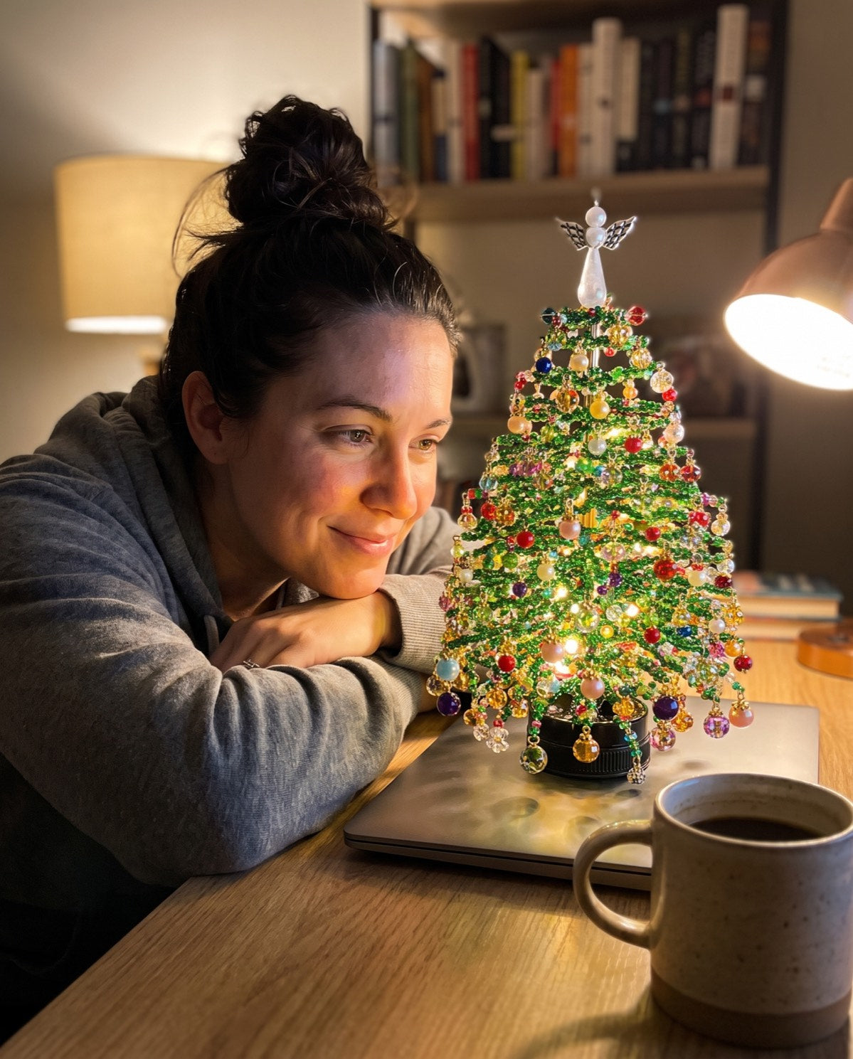 A finished beaded tree lit on a desk, its owner leaning in beside it
